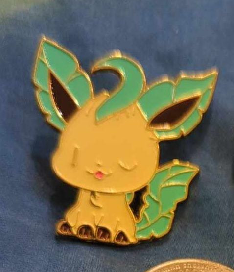 Two brooches with cartoon animal designs, one depicting a front view and the other a back view, set against a blue background.