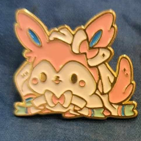 Two anime-style brooches depicting characters from the series, one is pink and the other is red, both with blue accents.